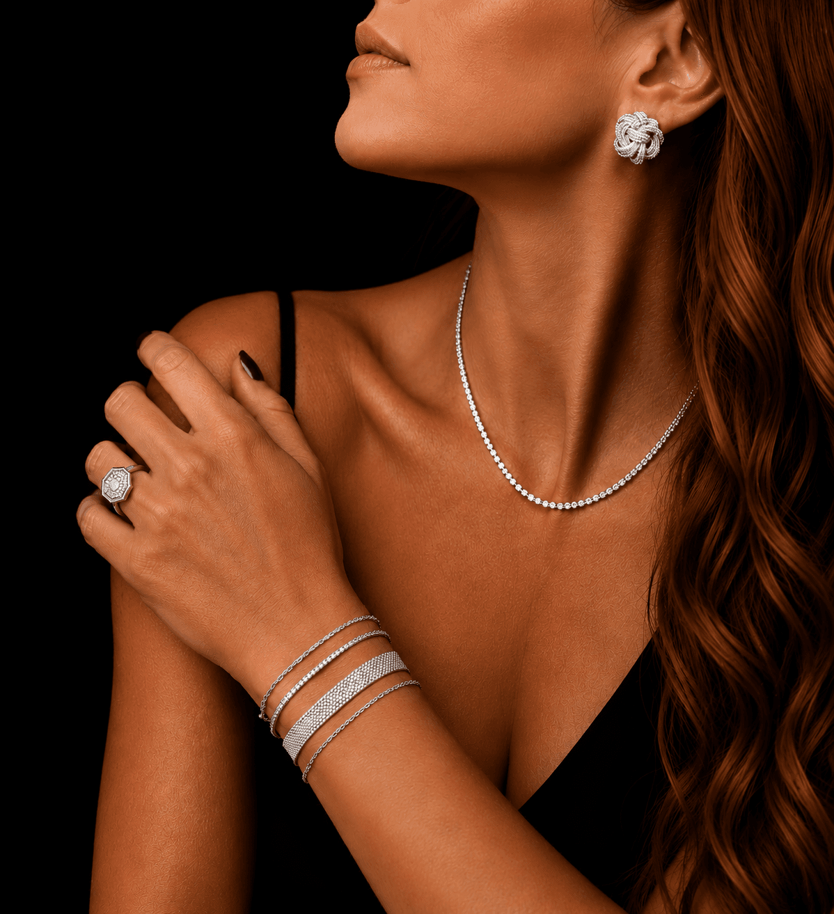 Modelo com a mão no próprio ombro, usando anel, pulseiras, colar e brinco de prata 925, fundo escuro.